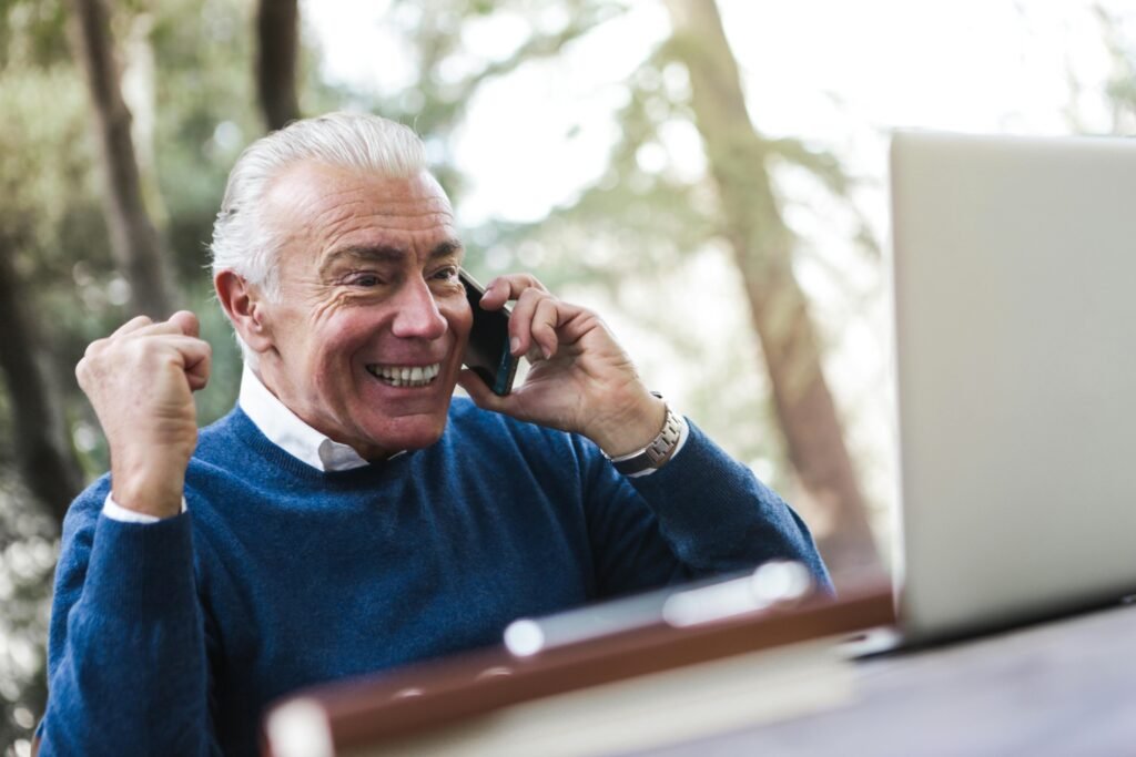 Older man on his phone looking at his computer smiling learning holiday affiliate marketing tips