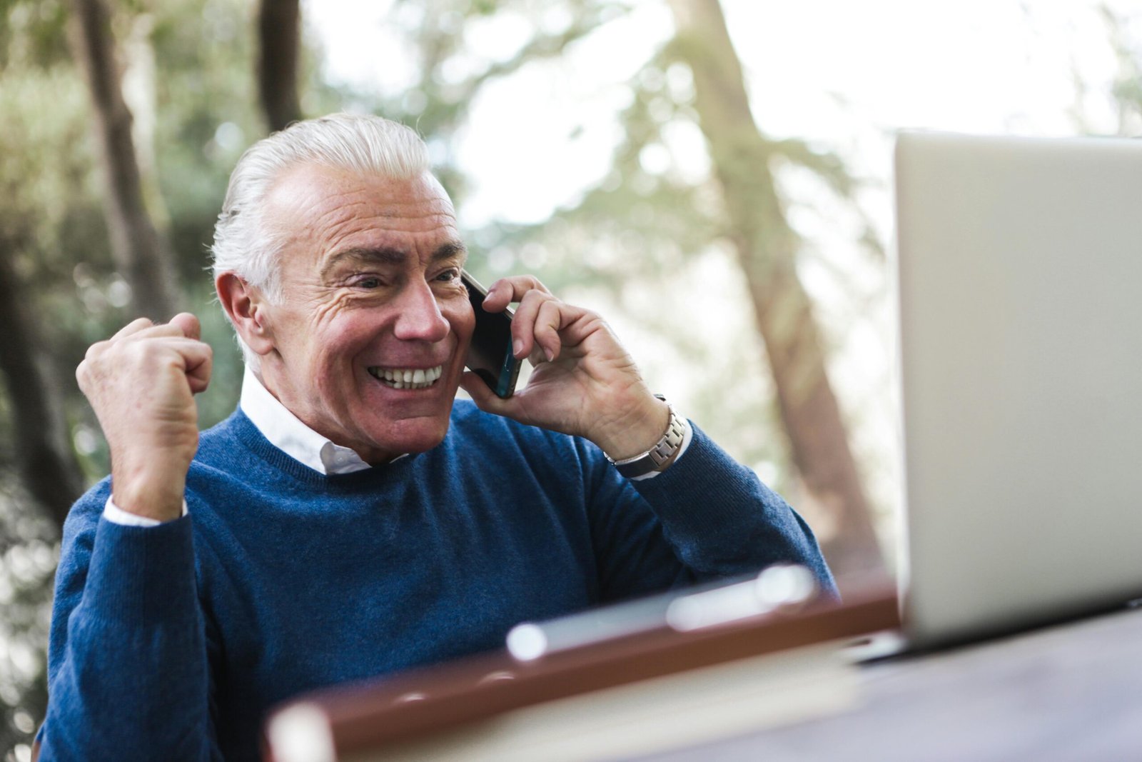 Older man on his phone looking at his computer smiling learning holiday affiliate marketing tips